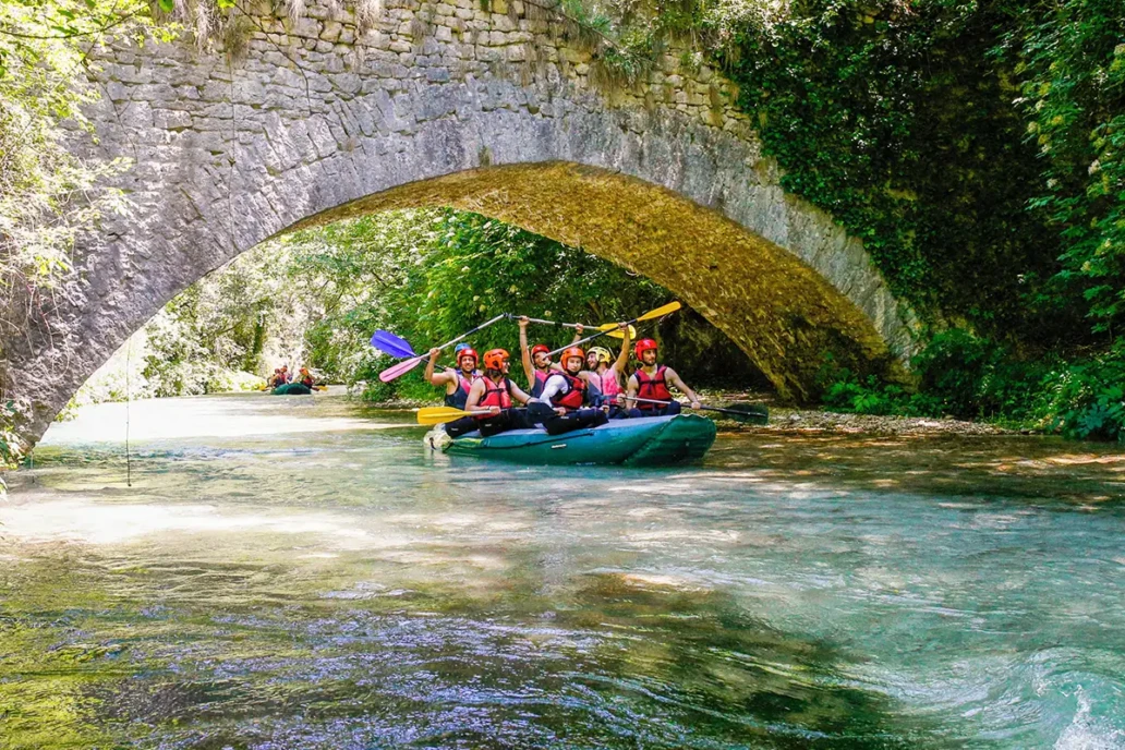 canoa di rafting mentre passa su un acqua cristallina e sotto ad un ponte