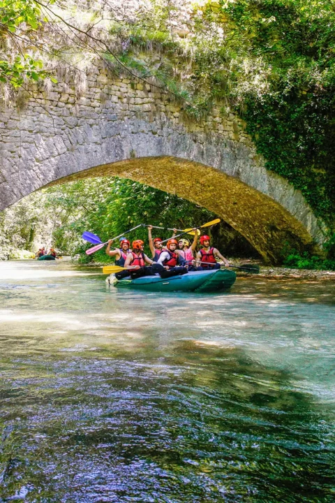 canoa di rafting mentre passa su un acqua cristallina e sotto ad un ponte