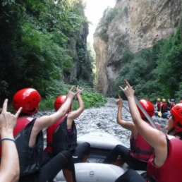 ragazza di spalle, su un gommone rafting in entrata nelle gole del fiume Corno, che fanno le corna con le braccia alzate